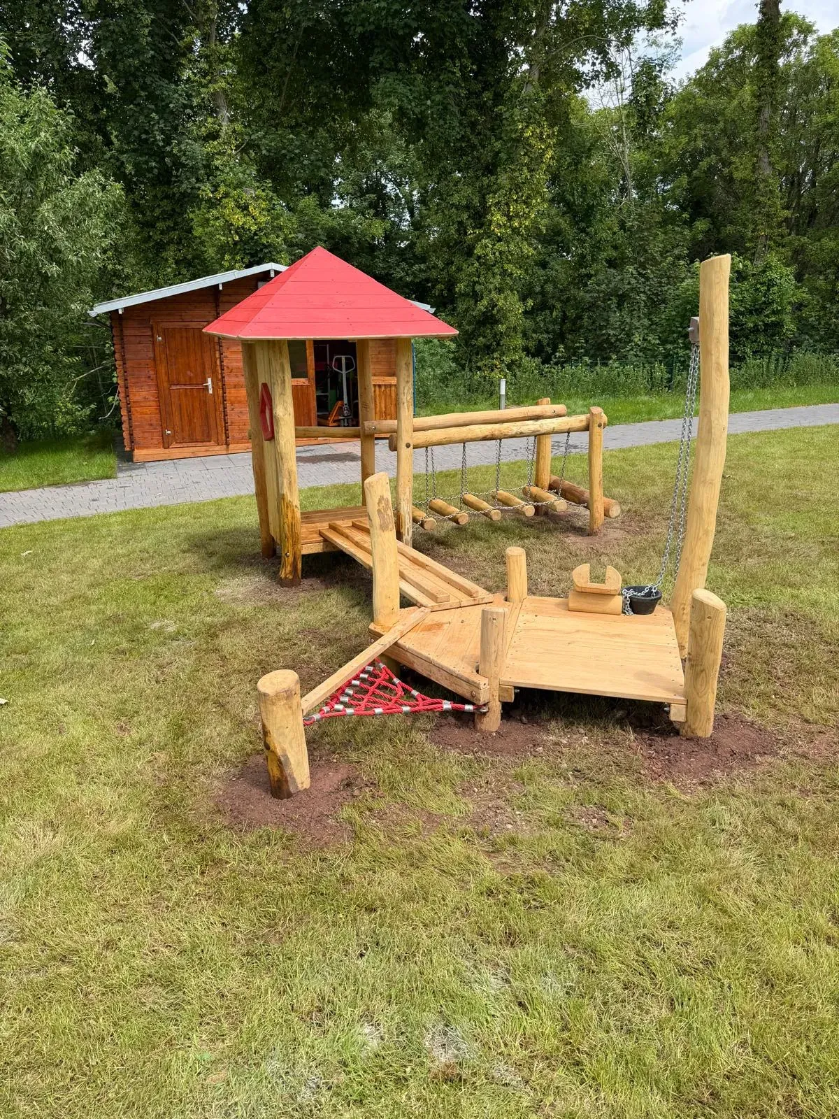 Spielhaus mit rotem Dach und Balancierelementen, montiert von Moshrif Spielplatzbau im Rurtal