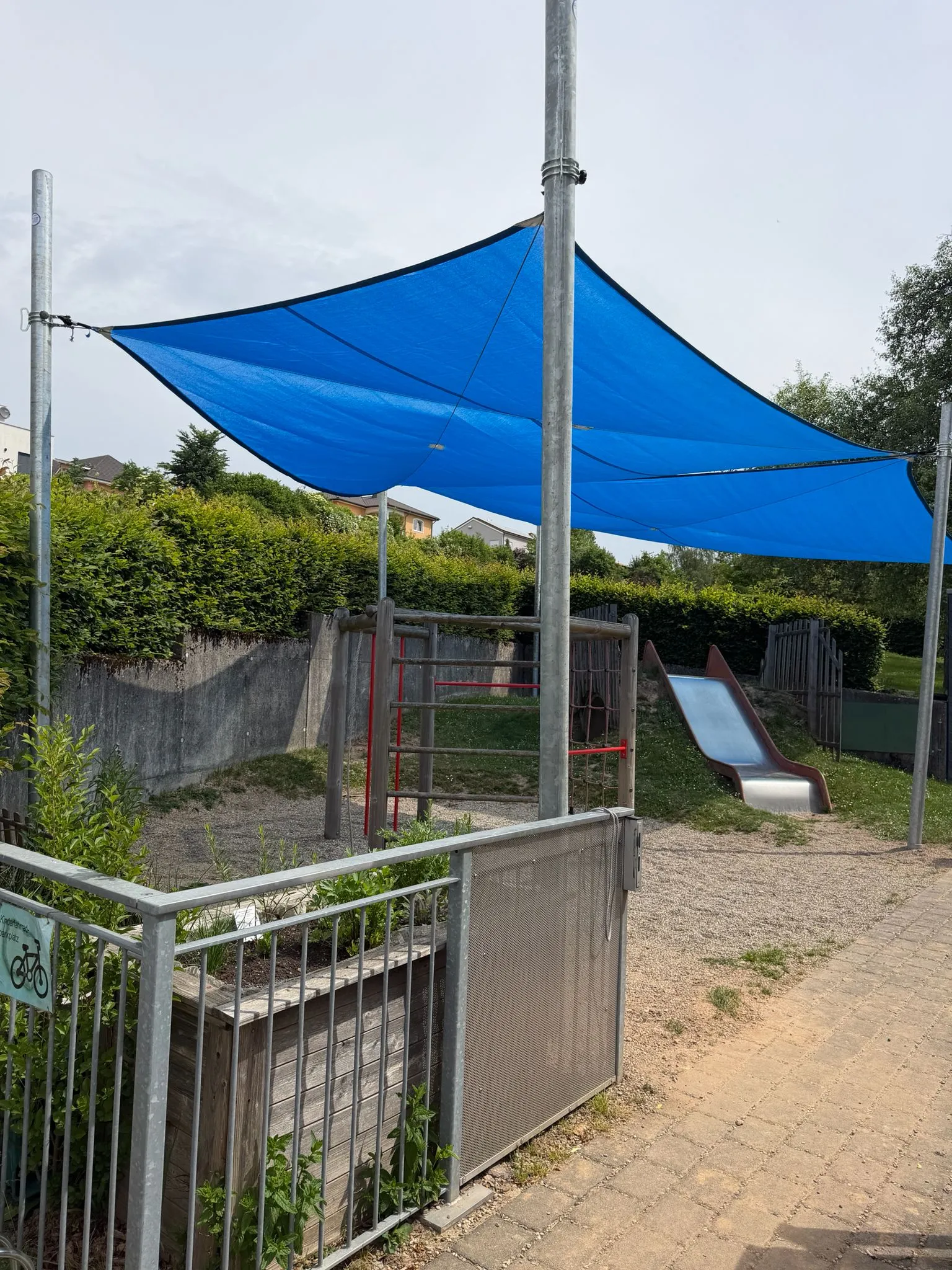 Blaue Sonnensegel beschatten einen Spielplatz mit Rutsche